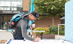 Student writing on a large piece of paper in front of the student union.